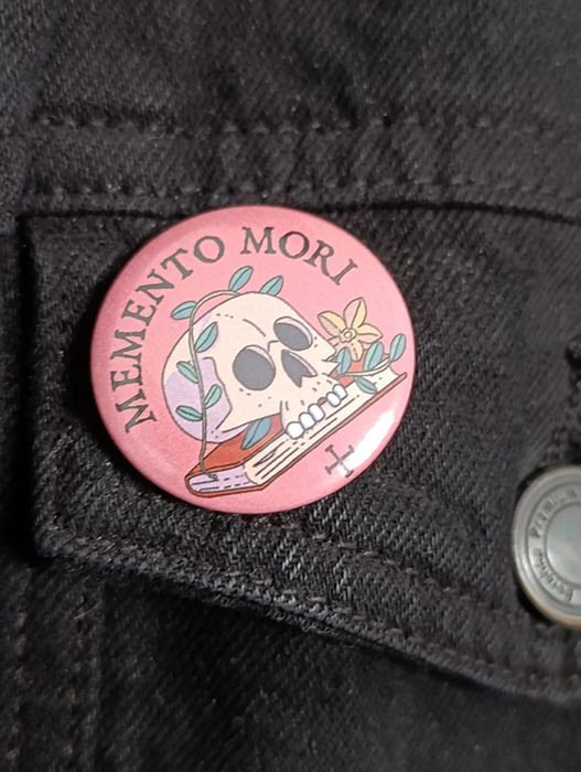 Chapa con una pequeña "Vanitas" representada con una calavera, flores y un libro. ¡Llévalas en tu bolso o chaqueta!